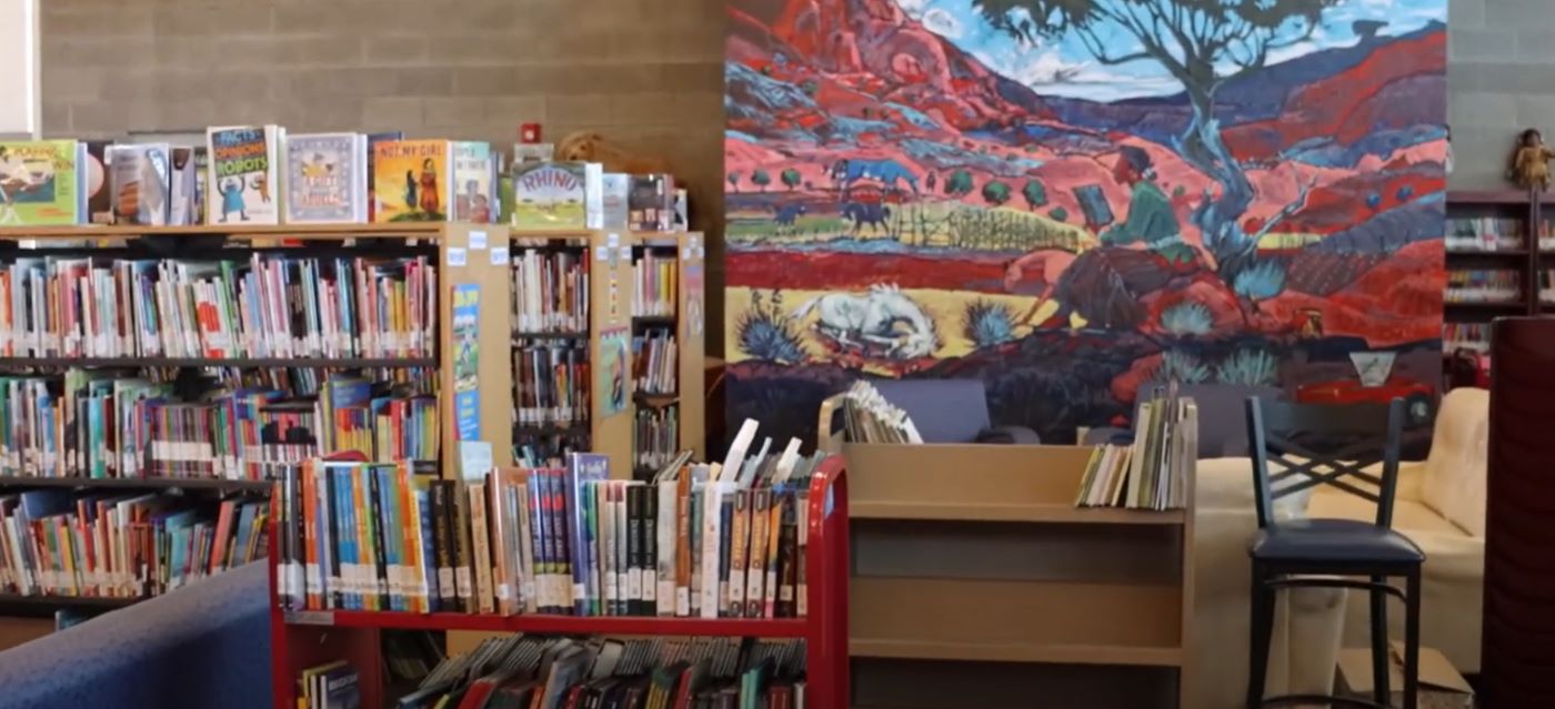 Tuba City Boarding School library filled with books, featuring a colorful painting hanging on the wall.