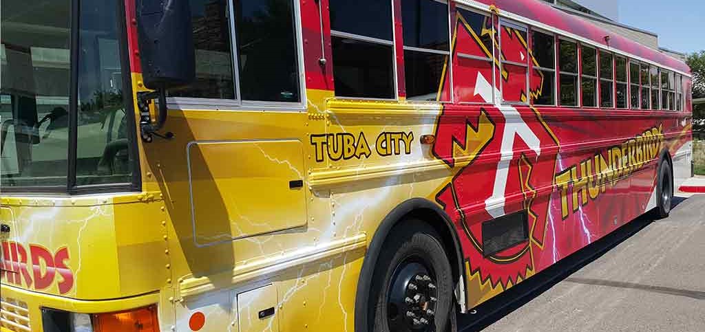 A bright red and yellow bus featuring a colorful design on the side with the text Tuba City Thunderbirds, ready for an exciting adventure.